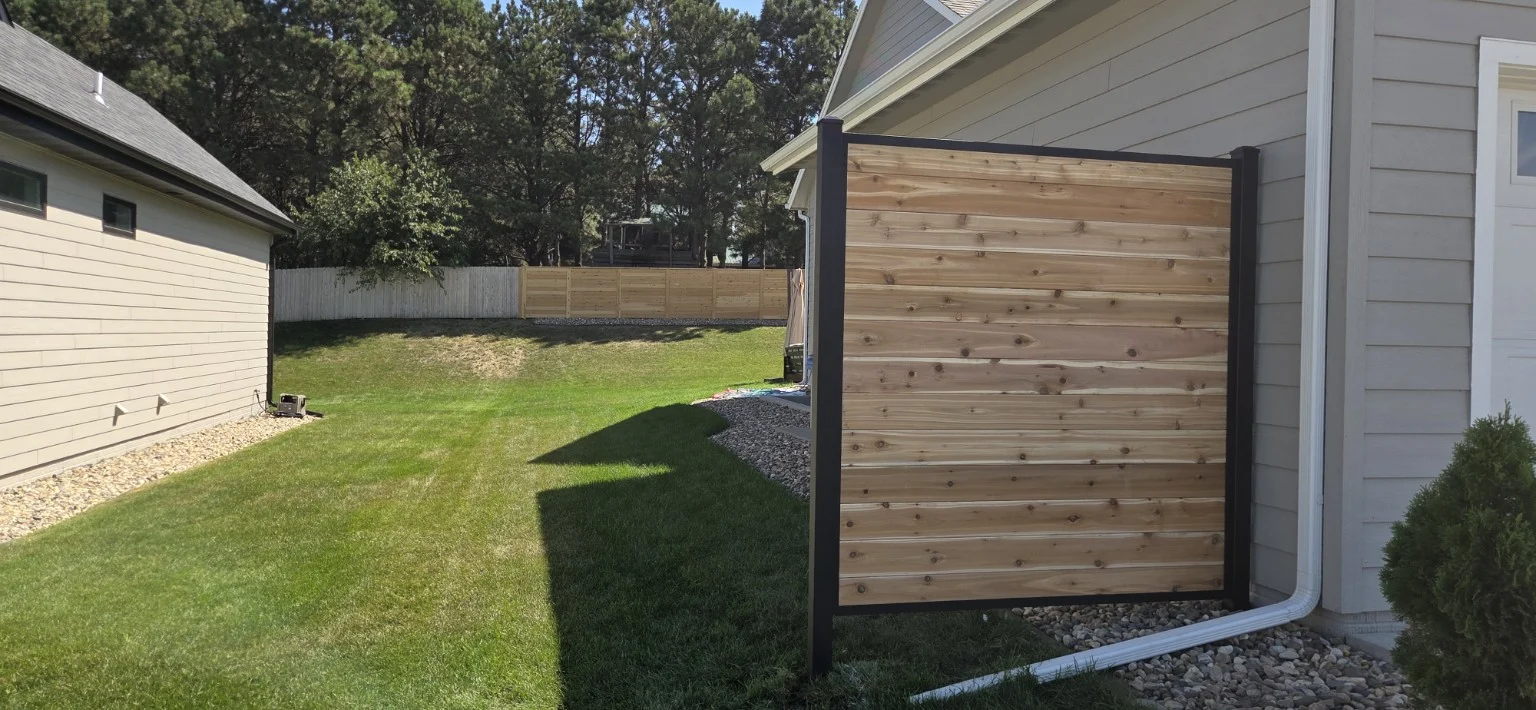 Single horizontal wood trash-bin screen with a black metal frame beside a Sioux Falls home